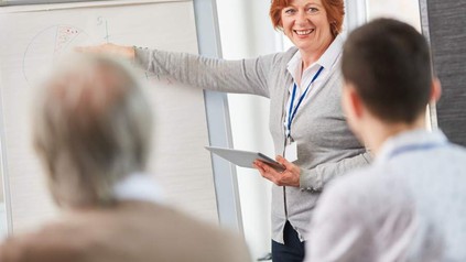 Eine Frau erklärt einigen Personen eine Grafik auf einem Flipchart