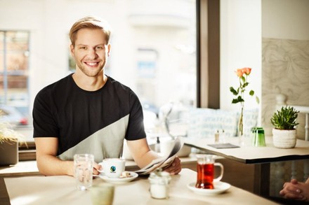 Ein junger Mann greift in einem Café eine Tasse Fairtradekaffee