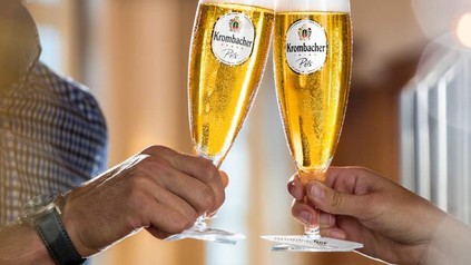 Zwei Personen stoßen mit Krombacher Pils in dazu passenden Gläsern an
