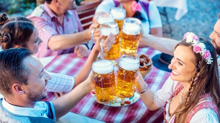 Junge Leute in Tracht stoßen in einem bayerischen Biergarten mit Bier-Masskrügen an