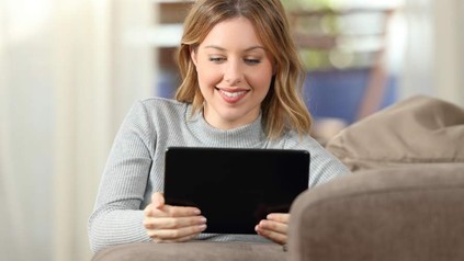 Eine junge Frau blickt lächelnd auf ihr Tablet