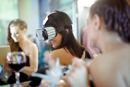 Eine Frau mit einer VR-Brille blickt ein Glas Wein an
