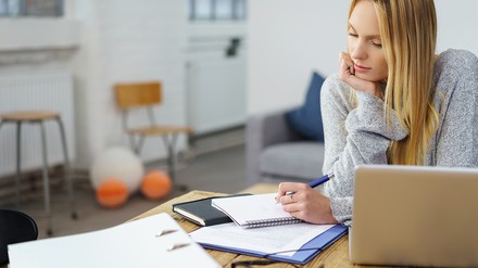 Junge Frau, Studentin, macht sich zu Hause Notizen vor aufgeklapptem Laptop