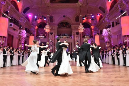 Männer in schwarzen Fracks und Frauen in weißen Kleidern tanzen im Kreis, umringt von Personen in derselben Kleidung