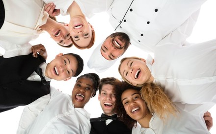 Köche und Servicekräfte halten sich lachend gegenseitig im Arm