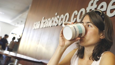 Junge Frau trinkt aus einem Kaffeebecher in einem Coffee Shop der Kette San Francisco Coffee Company