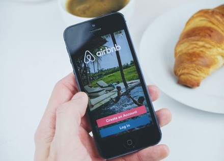 Eine Person hält ein Smartphone auf dem die Airbnb App aufgerufen ist