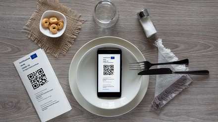 Gedeckter Tisch auf dem ein Smartphone mit geöffnetem Impfausweis liegt