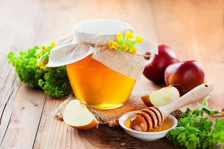 Ein liebevoll dekoriertes Gläschen in dem sich eine orangene Flüssigkeit befindet, daneben Honig Äpfel und Sellerie