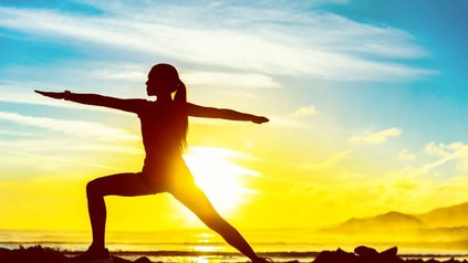 Eine Frau praktiziert Yoga vor dem Sonnenaufgang am Strand