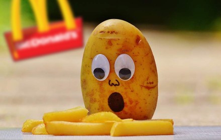 Eine Kartoffel mit Glupschaugen und einem offenen Mund blickt erstaunt auf ein paar Pommes