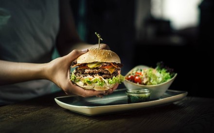 Eine Person richtet einen Burger auf einem Teller mit Salat an