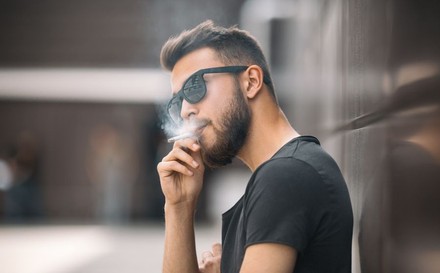 Junger bärtiger Mann mit Sonnenbrille raucht Zigarette