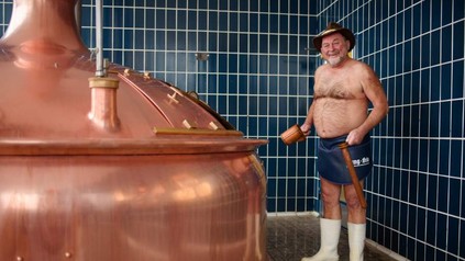 Jürgen Hopf nur mit Gummistiefeln, Hut und Lendenschurz bekleidet beim Bierbrauen