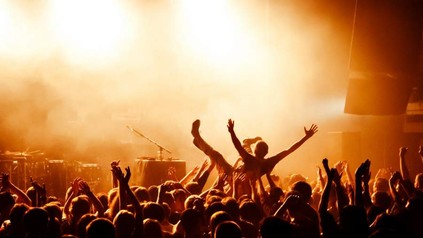 Ein Mann beim Crowdsurfing vor einer Bühne mit hunderten von Zuschauern