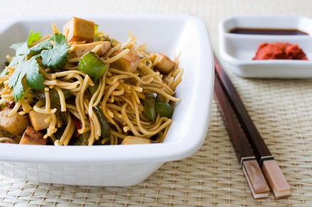 Ein Teller mit Nudeln mit Tofu und Gemüse und Essstäbchen