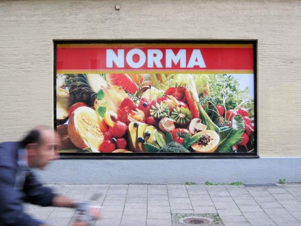 Ein Plakat von Norma mit diversem Gemüse und Obst an einer Hauswand