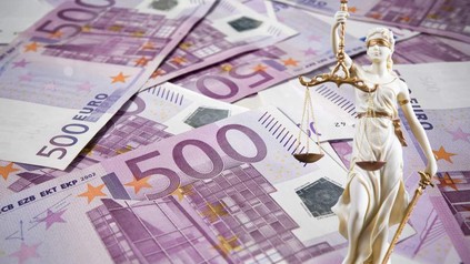 Eine Justitia Statue steht vor mehreren 500€ Scheinen