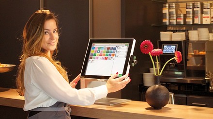 Blonde junge Frau mit weißem Hemd steht an einem Kassenterminal im Restaurant