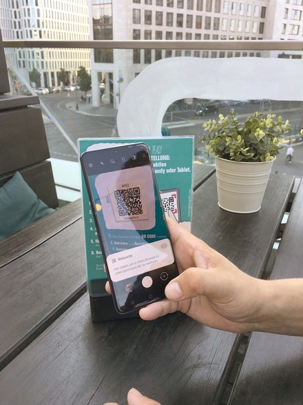 Hand scannt einen QR-Code mit dem Smartphone, der auf einem Tischaufsteller aufgedruckt ist
