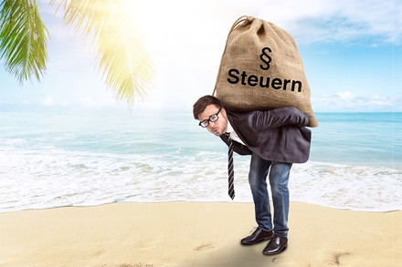 Ein Mann am Strand trägt einen Sack, auf dem Steuern steht.