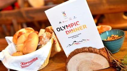 Ein gedeckter Frühstückstisch auf dem eine Proschüre platziert ist auf der Olympic Dinner steht