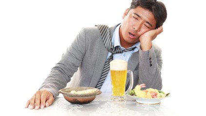 Müder Asiate sitzt vor Bier und Essen