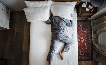 Mann liegt mit Kopf unter dem Kissen auf Bett