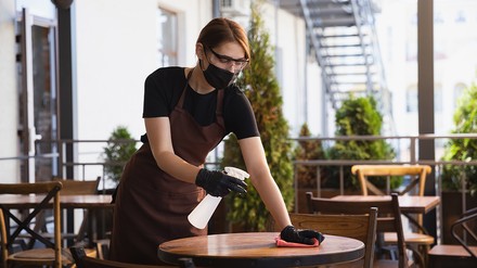 Kellnerin mit Mund-Nasen-Schutz desinfiziert einen Tisch