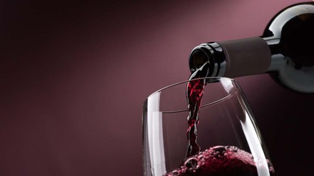 Rotwein wird vor lila Hintergrund in Weinglas geschenkt