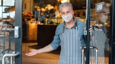 Gastronom mit Mundschutz bittet herein