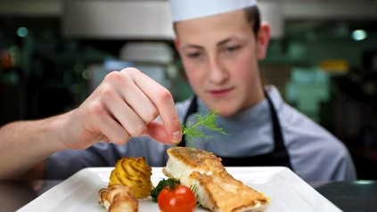 Ein Koch dekoriert einen angerichteten Fisch auf einem Teller