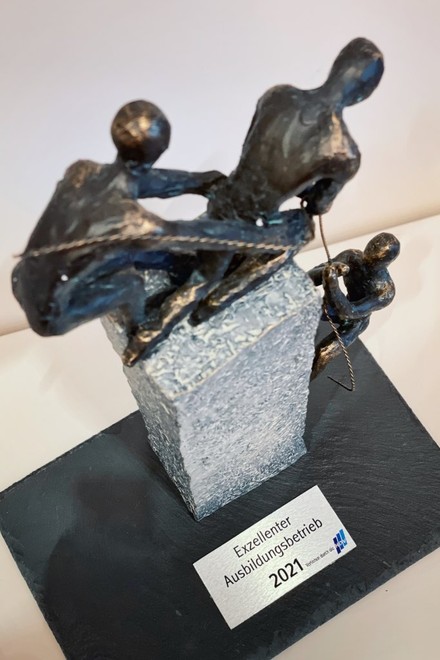 Nahaufnahme des Exzellente Ausbildungsbetrieb-Awards 2021, der aus zwei Kupferfiguren, die einer dritten beim Besteigen eines Granitblocks helfen