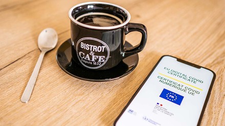 Impfnachweis, geöffnet auf dem Smartphone, liegt neben einer gefüllten Kaffeetasse