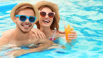 Ein Mann und eine Frau im Pool lachen in die Kamera. Die Frau hält einen Cocktail in der Hand.
