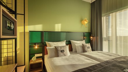 Minimalistisch eingerichtetes Hotelzimmer mit grüner Wand und großer Fensterfront