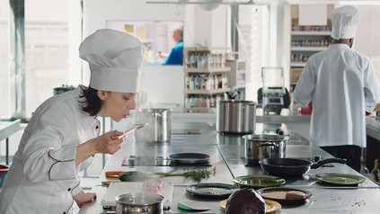 Eine Frau steht am Herd und probiert eine Soße.