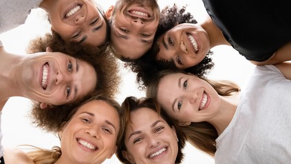 Menschen stehen in einem Kreis zusammen, haben die Köpfe zusammengesteckt und lächeln.