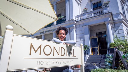 Joy Ewulu vor dem Hotelschild des "Hotel Mondial"
