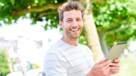 Ein junger Mann mit Ipad in der Hand lächelt in die Kamera.