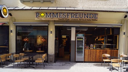 Pommes Freunde Filiale von außen mit Biertischen und Bierbänken