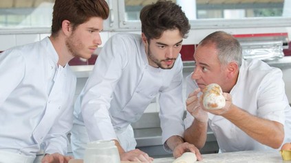 Ein Bäcker zeigt seinen Lehrlingen ein Brot