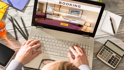 Ein Mann sitzt an einem Laptop auf dem eine Hotelbuchungsseite geöffnet ist
