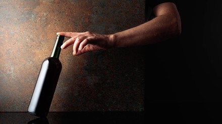 Eine Hand greift nach einer Weinflasche.