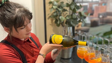 Yvonne Göttlinger mit Sektflasche beim Zubereiten eines Aperol Spritz