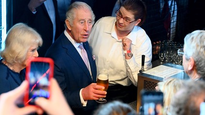 König Charles III. von Großbritannien hält neben Königsgemahlin Camilla ein selbst gezapftes Bier in der Hand