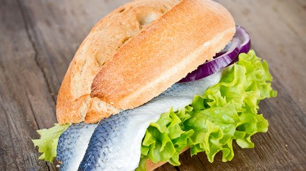 Ein frisch belegtes Brötchen mit Bismarckhering, Salat und Zwiebelringen.