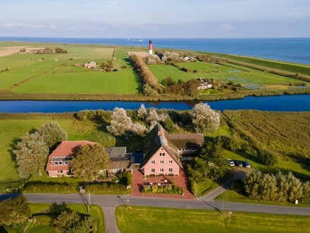 Vom Restaurant des Hotels mit angrenzender Terrasse Von einigen Zimmern und dem großzügigen Garten hinter dem Hotel hat man einen traumhaften Blick auf den rot-weiß gestreiften Pellwormer Leuchtturm. Auf der anderen Seite einen malerischen Sonnenuntergang mit Lämmern und wolligen Schafen im Horizont. (Foto: © MEDIAteria-Ines Preißer)