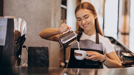 Weibliche Barista schüttet Milch in eine Tasse