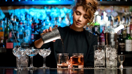 Eine Bartenderin bereitet hinter der Bar einen Cocktail zu.